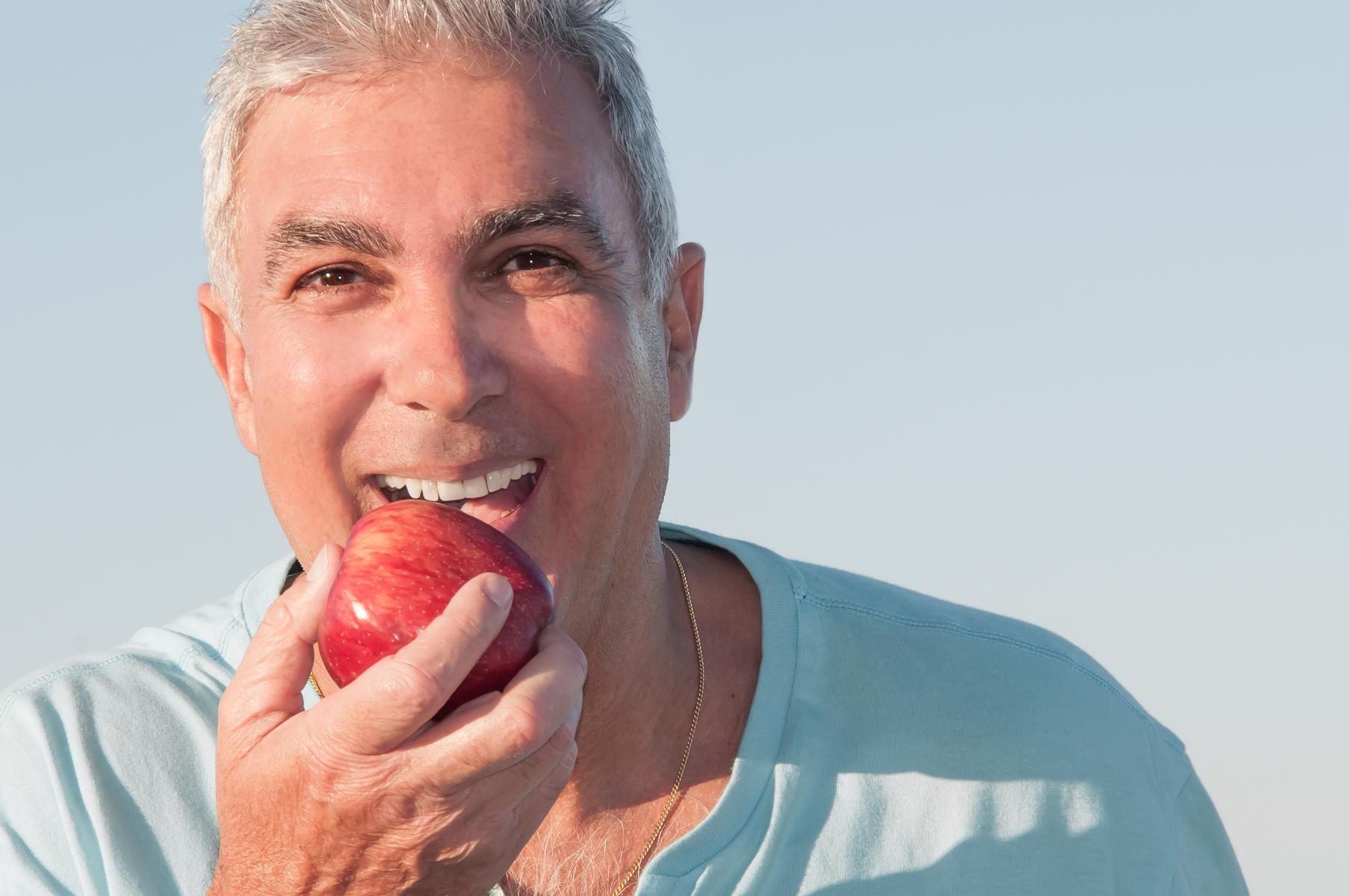 man biting apple and smiling showing teeth